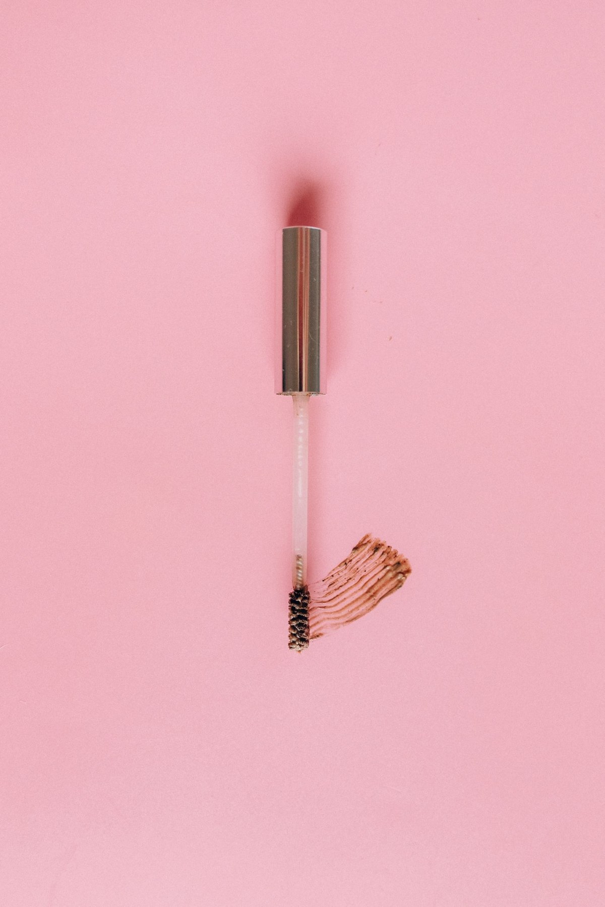 An open mascara wand against a pink background