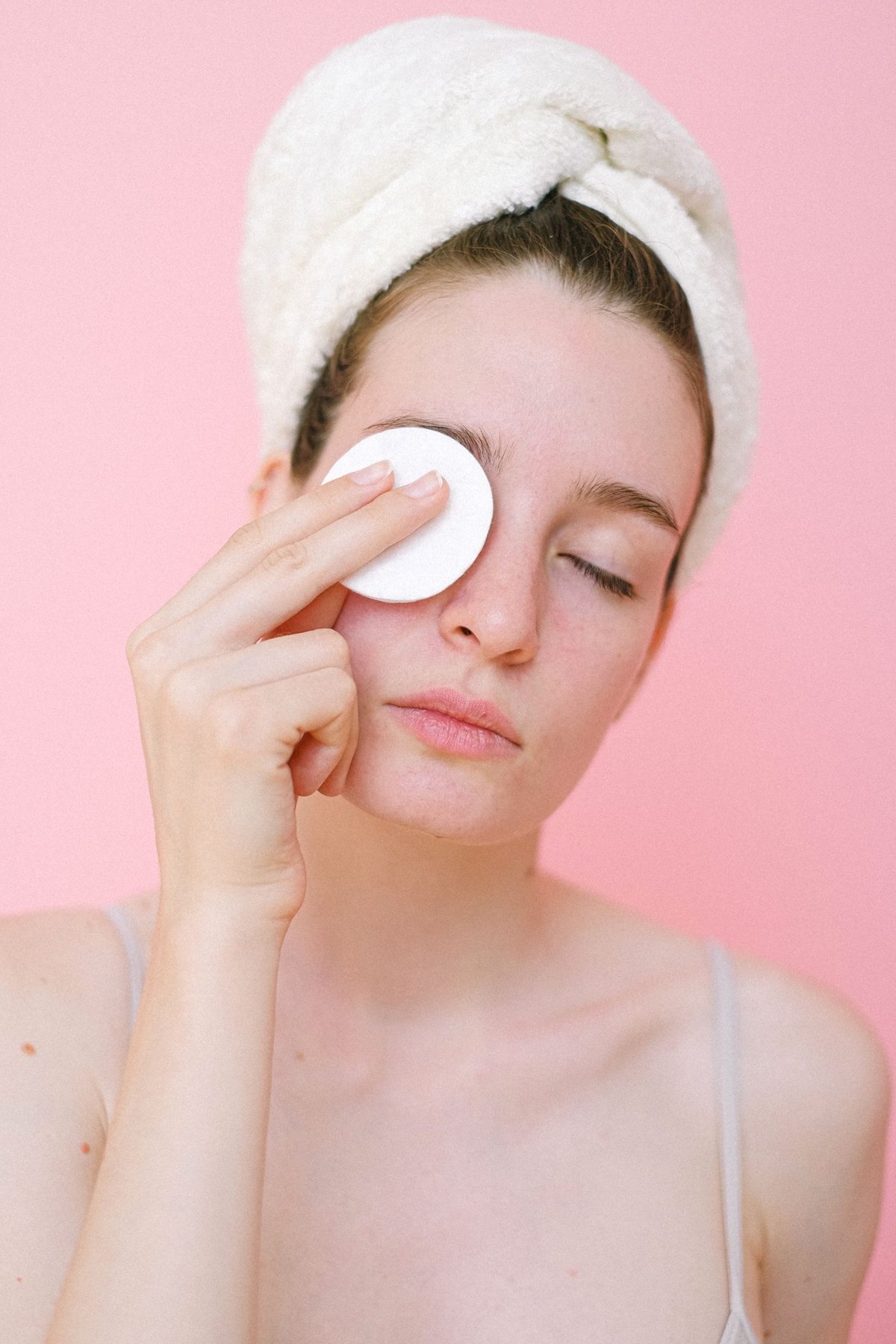 A woman removes eye makeup with a cotton pad