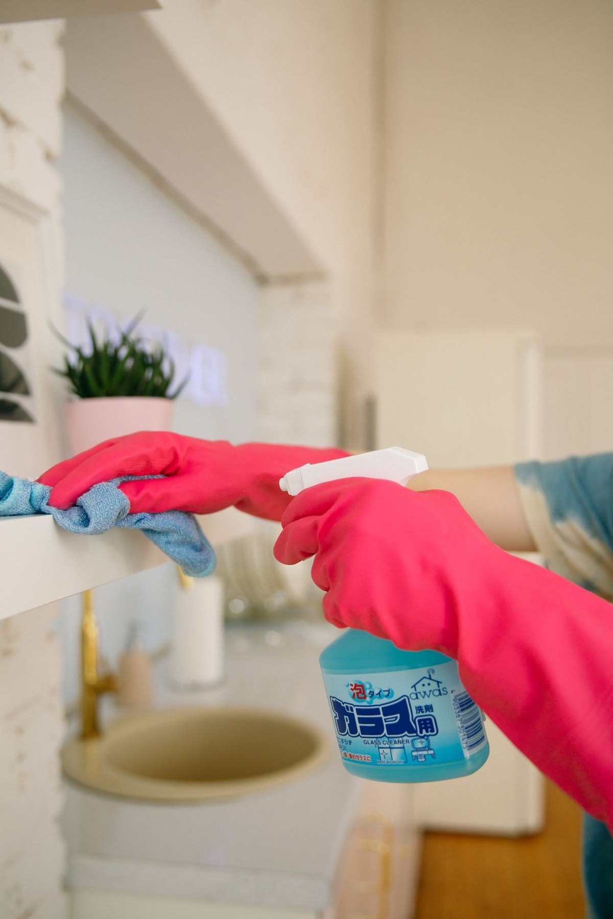 A person wipes a shelf with a cloth and spray cleaner