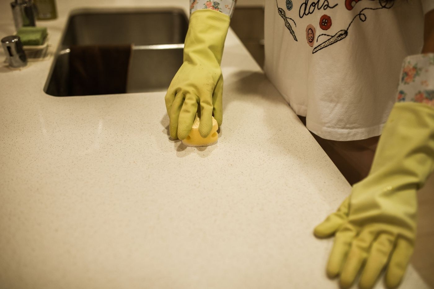 Gloved hands wipe a kitchen worktop with a sponge