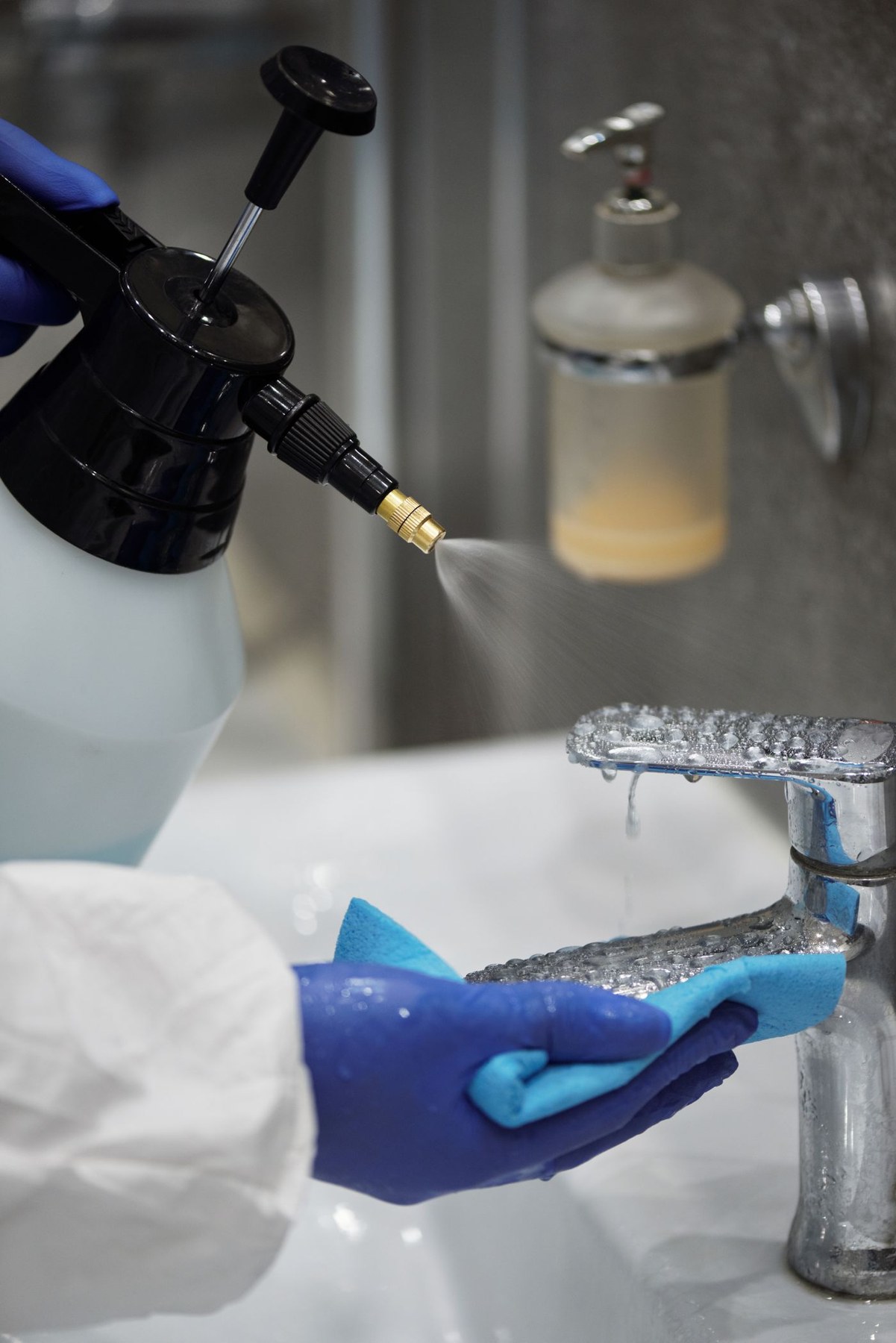 A gloved hand holds a cloth beside a faucet while cleaner is sprayed
