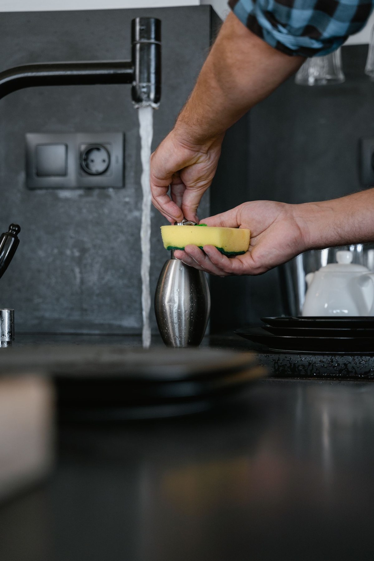 Hands hold a sponge beside a kitchen faucet